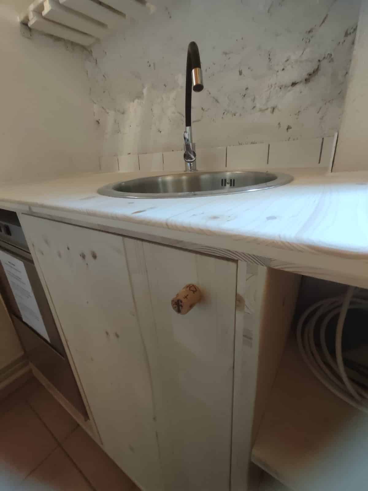 Cuisine rustique bois clair avec évier inox et robinet noir Évier inox sur bois clair avec robinet noir et poignée originale en bouchon de liège.